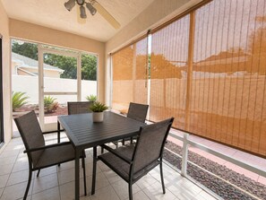 A covered patio with a table and chairs, a ceiling fan, and a view through large windows. - Alfredo Retreat at Spanish Springs (The Villages)