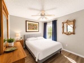 A bedroom with a bed, a ceiling fan, a nightstand with a lamp, a mirror, and a painting on the wall. - Alfredo Retreat at Spanish Springs (The Villages)