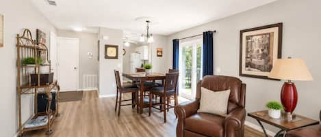 A spacious living room with a brown leather sofa, a dining area with a wooden table and chairs, and a kitchen in the background.