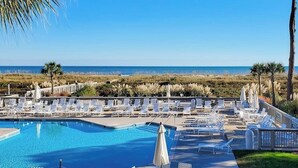 Ein Poolbereich mit Liegestühlen und Sonnenschirmen mit Blick auf einen Strand und das Meer.