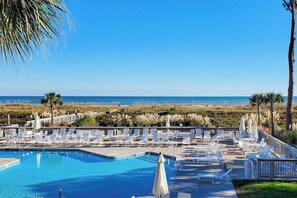 Ein Poolbereich mit Liegestühlen und Sonnenschirmen mit Blick auf einen Strand und das Meer.