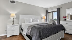 Ein Schlafzimmer mit einem Bett, zwei Nachttischen, einer Kommode, einem Fenster mit Vorhängen und Blick.