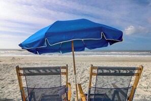 Dos sillas de playa con una sombrilla azul sobre arena.
