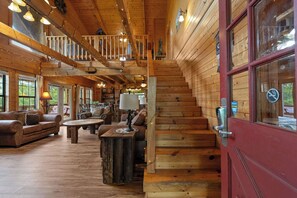 Ein Holzblockhaus-Innenraum mit einer Holztreppe, einer roten Tür und einer gemütlichen Sitzecke mit Sofa und Couchtisch.