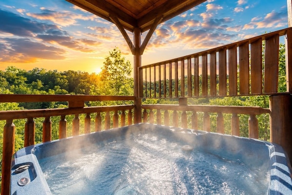 Ein Whirlpool auf einer Holzterrasse mit Blick auf einen Sonnenuntergang und Bäume.