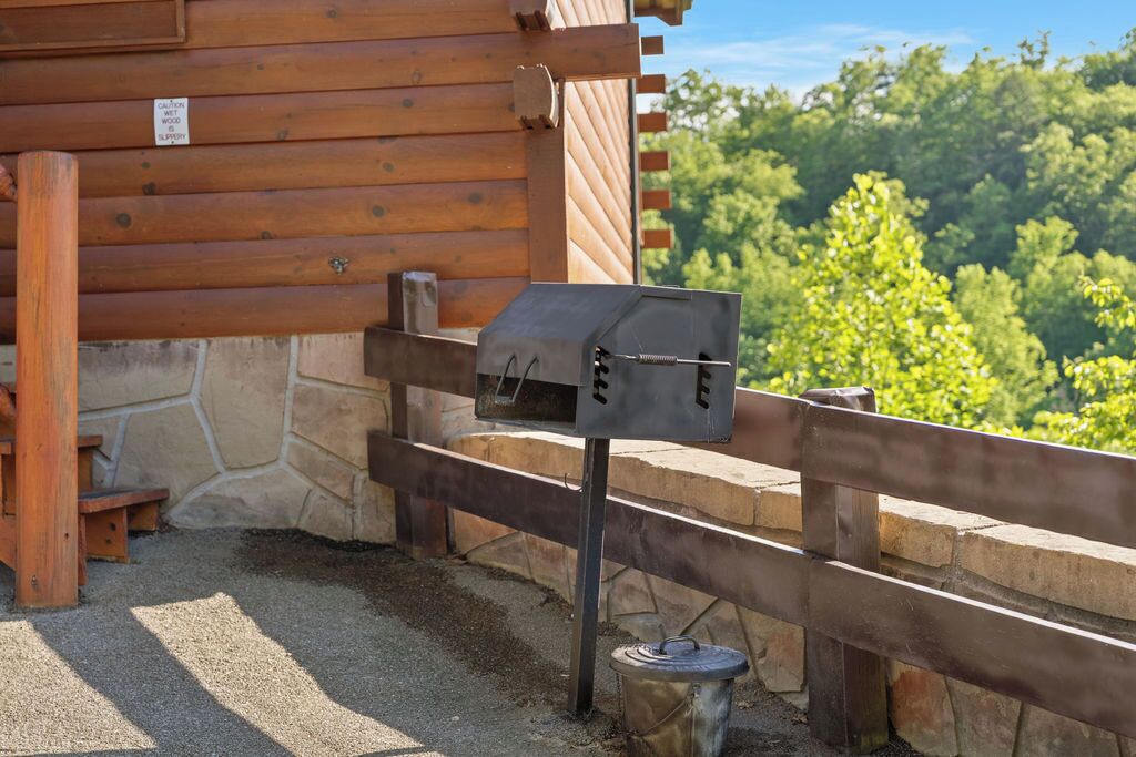 Een houten hutje met een metalen barbecue aan de buitenmuur, een stenen fundering en een grindpad.