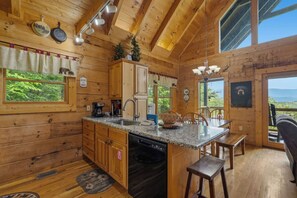 Eine Holzhütte mit Küche, ausgestattet mit Granit-Arbeitsplatten, Holzschränken und einem großen Fenster mit Blick auf Grünflächen.