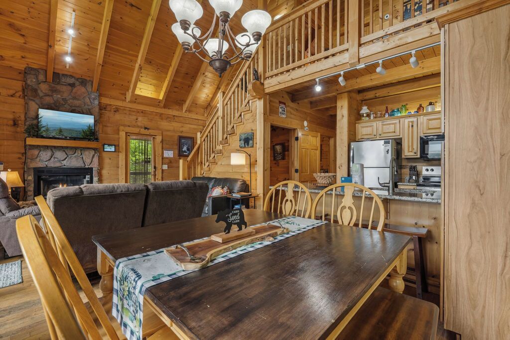 A wooden cabin interior with a dining area, kitchen, fireplace, and a balcony.