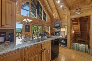 Eine Blockhütte mit Küche, ausgestattet mit Granitarbeitsplatten, Holzausstattung, einem Kamin aus Naturstein und einem großen Fenster.