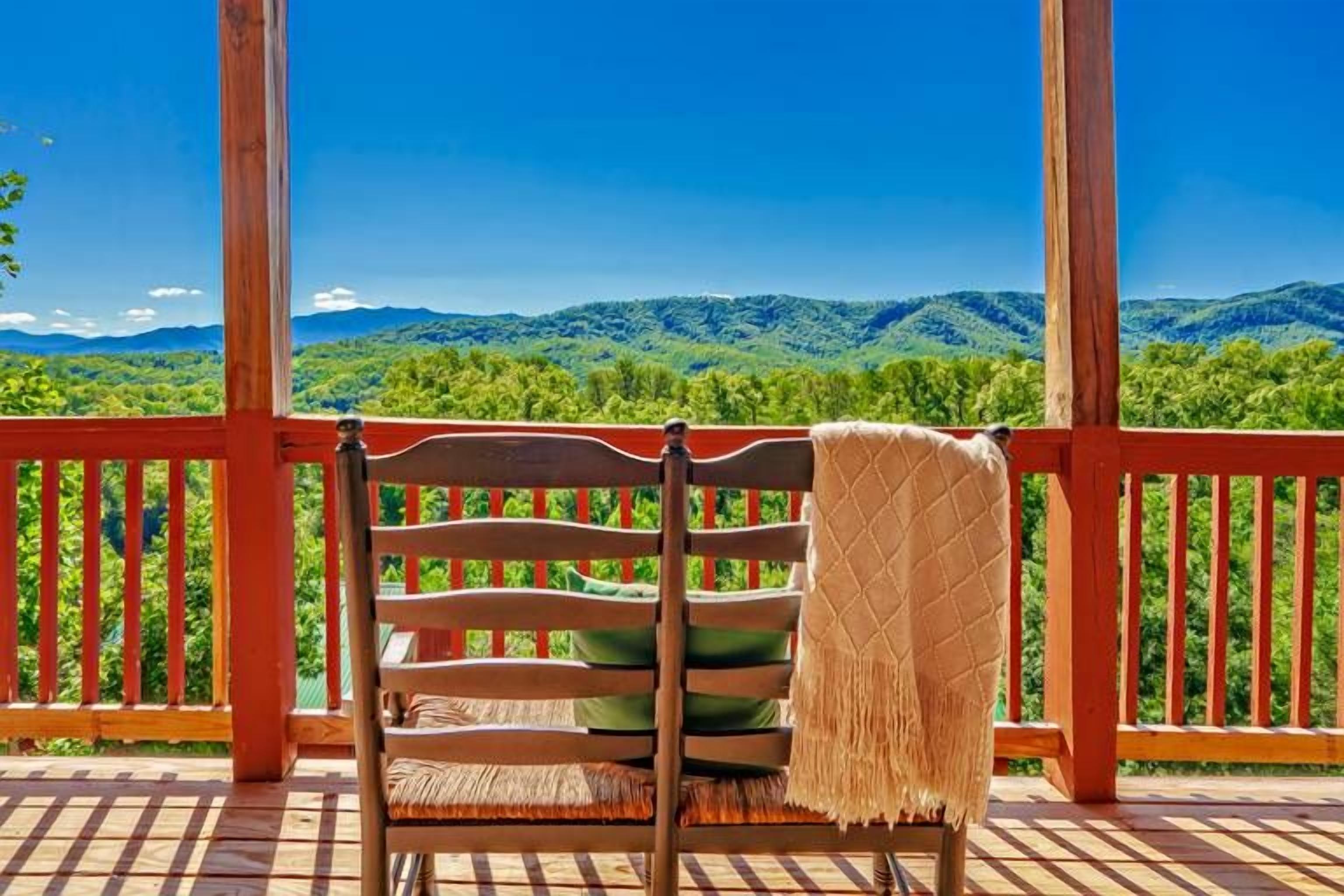 A wooden deck with a wooden chair and a blanket, overlooking a mountainous landscape.