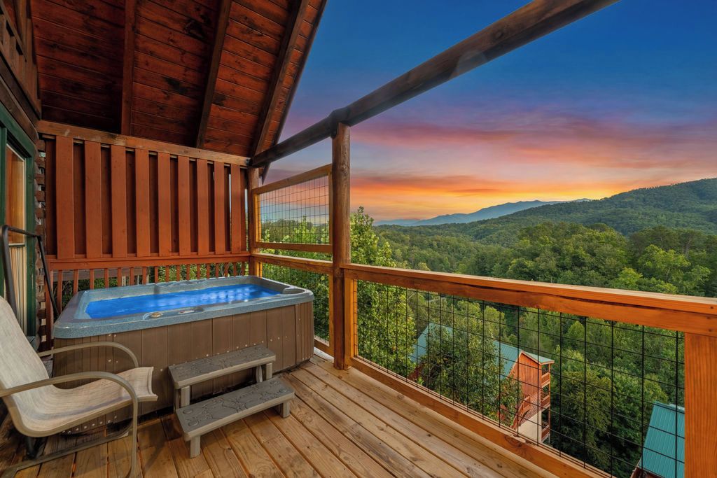 A wooden deck with a hot tub and seating, overlooking a forested landscape.