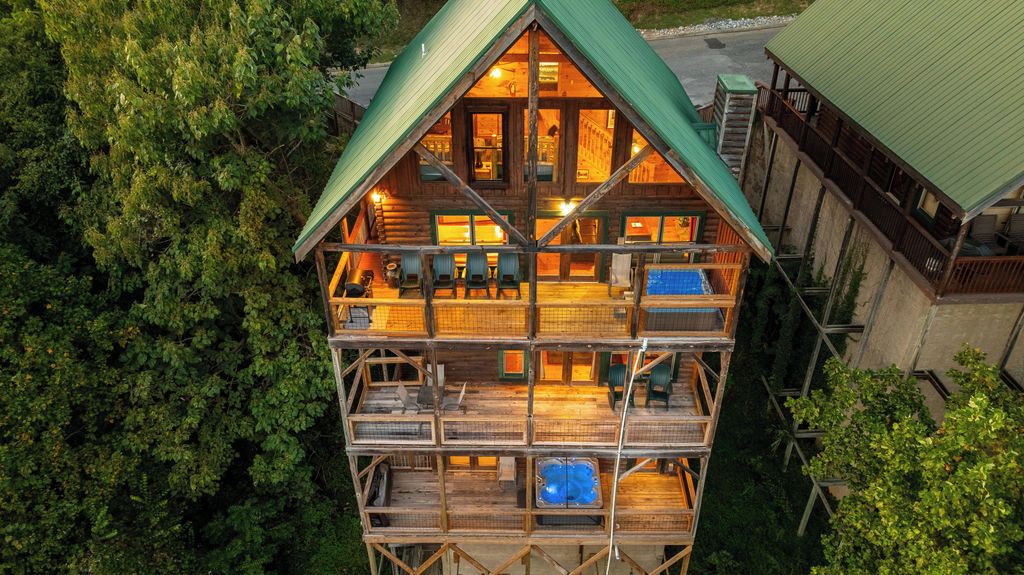 Une cabane en rondins à plusieurs étages, dotée d’un balcon à l’étage supérieur, et entourée d’une forêt dense.