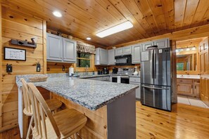 A wooden cabin interior with a kitchen featuring granite countertops, a stainless steel refrigerator, and wooden cabinets. - Amazing Rocky Top Views: Vistas That Wow (Pigeon Forge)