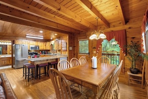 A wooden cabin interior with a dining area, kitchen, and a large window overlooking greenery. - Forget Me Not: Memories You'll Never Forget (Pigeon Forge)