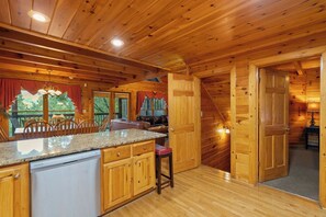 A wooden cabin interior with a kitchen area, dining space, and a staircase leading to another level. - Forget Me Not: Memories You'll Never Forget (Pigeon Forge)