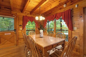 A wooden dining room with a large table and chairs, a chandelier, and windows with red curtains. - Forget Me Not: Memories You'll Never Forget (Pigeon Forge)