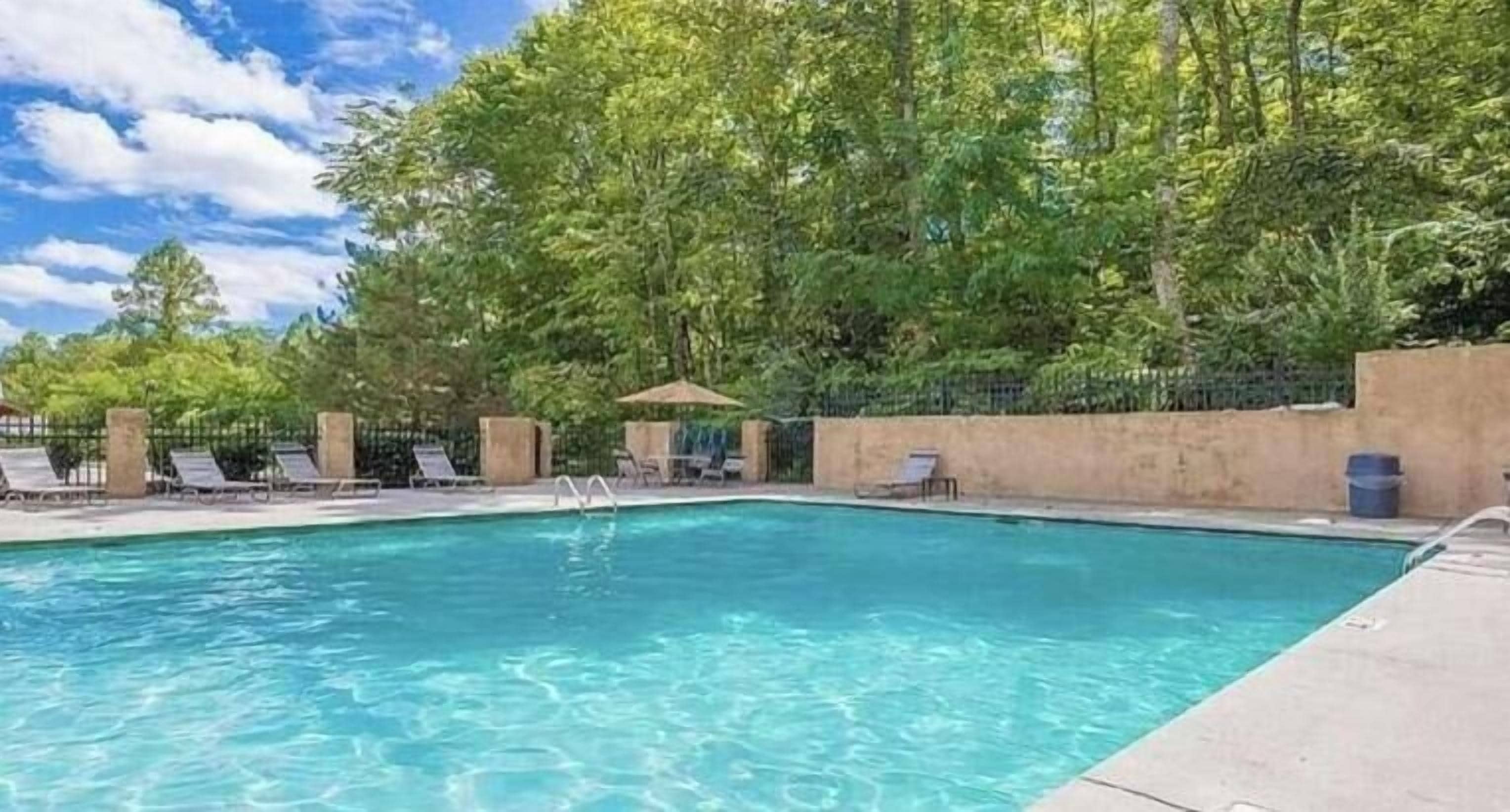 A swimming pool with lounge chairs and a fence, surrounded by trees.
