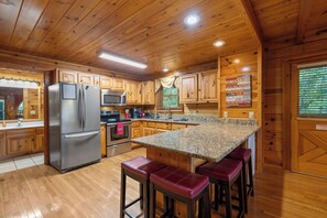 A wooden-paneled kitchen with a granite countertop, stainless steel appliances, and a bar area with stools. - Forget Me Not: Memories You'll Never Forget (Pigeon Forge)