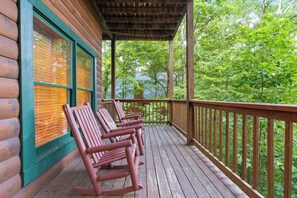 A wooden deck with rocking chairs and a covered area overlooking a forested landscape. - Forget Me Not: Memories You'll Never Forget (Pigeon Forge)