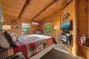 Une chambre dans un chalet en bois, comprenant un lit, deux fenêtres, une cheminée, un téléviseur et un extincteur.