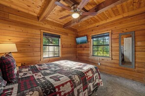 A wooden cabin bedroom with a bed, a ceiling fan, two windows, and a television. - Ridge Retreat: Life's Better on the Ridge (Pigeon Forge)