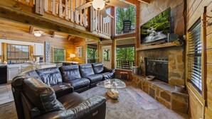 Un amplio salón con sofá de cuero, chimenea y televisión.