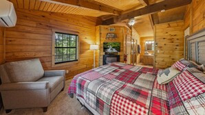 Una habitación de cabaña acogedora con una cama, una silla, un televisor y una ventana.