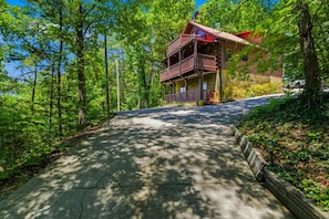 Eine Hütte mit Steinaußenwand, einer Holzterrasse und einer Auffahrt zum Eingang.