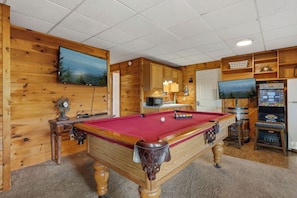 A pool table in a room with wooden walls, a television mounted on the wall, and a bar area with arcade games. - Ridge Retreat: Life's Better on the Ridge (Pigeon Forge)