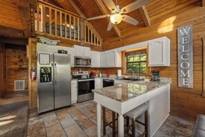 L’intérieur d’un chalet en bois comprend une cuisine avec un îlot central, un ventilateur de plafond et un panneau d’accueil.