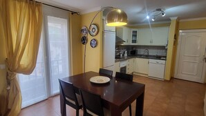 Un comedor con una mesa y sillas, una cocina con armarios blancos y un ventanal corredero.