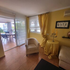 A living room with a sofa, armchair, and a small table with a candle holder. There is a sliding glass door leading to an outdoor area with a table and chairs. - El Rincon 5 - spacious apartment in beautiful complex (Los Cristianos)