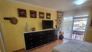Un dormitorio con cama, cómoda, televisor y balcón con mobiliario exterior.