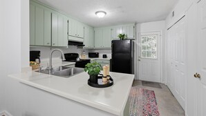 Une cuisine avec des plans de travail blancs, des meubles de rangement verts, un réfrigérateur noir et une porte blanche.