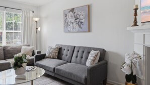 Un salon avec un canapé gris, une table basse en verre, une œuvre d’art florale encadrée et une orchidée en pot.