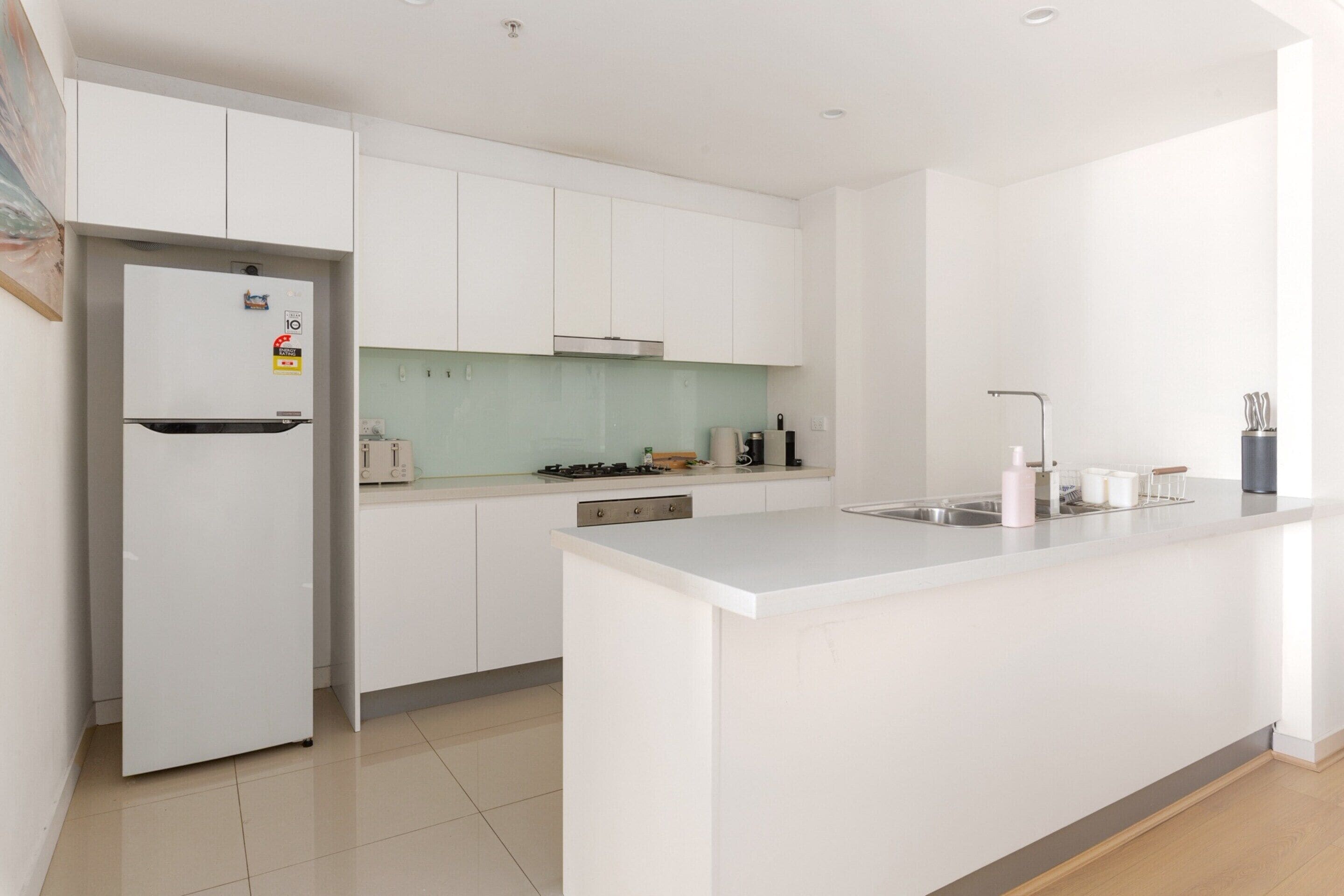 Una cocina moderna con armarios blancos, una isla integrada y un refrigerador de acero inoxidable.