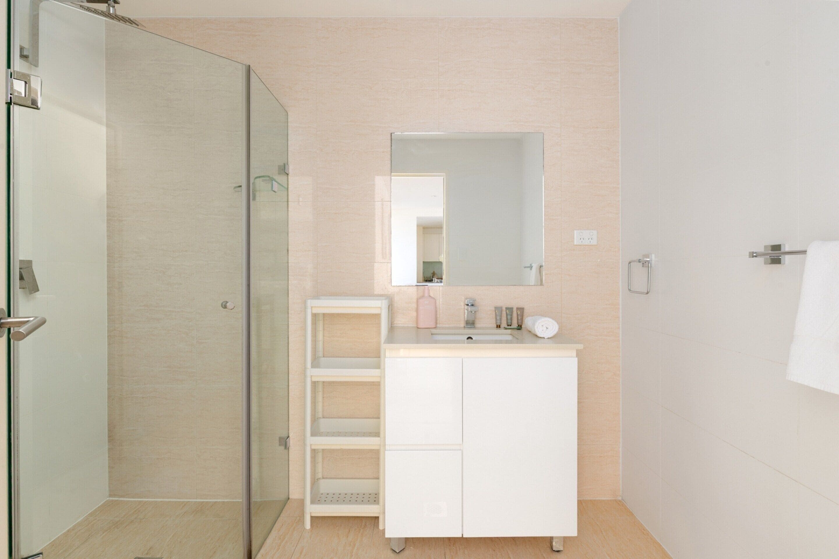 Un baño moderno con cabina de ducha de vidrio, tocador blanco con espejo y una toalla colgada en la pared.