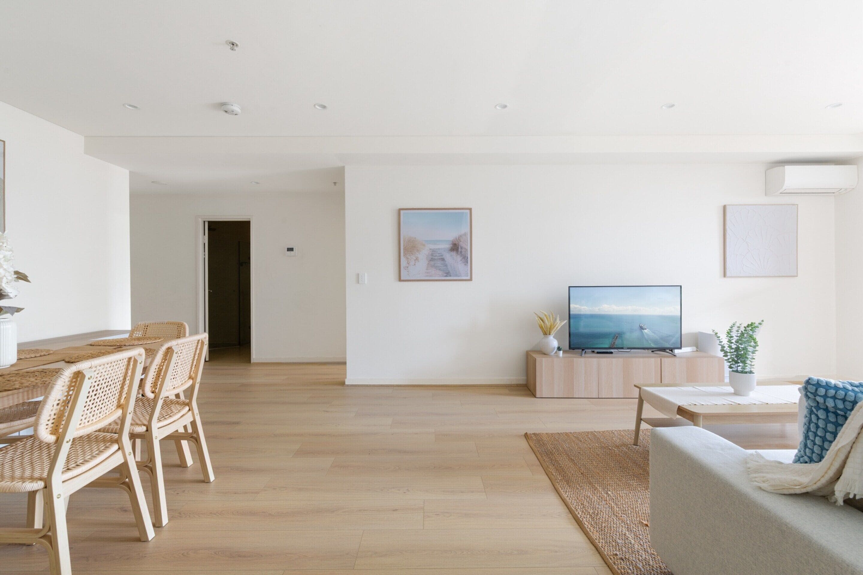 Un amplio espacio de sala de estar con una mesa de comedor de madera, sillas de mimbre, un sofá, un televisor y un cuadro en la pared.