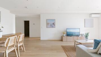 Un amplio espacio de sala de estar con una mesa de comedor de madera, sillas de mimbre, un sofá, un televisor y un cuadro en la pared.