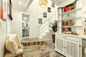 Ein modernes Interieur mit einer Treppe, einer Sitzecke mit Kissen, einem Schrank mit Dekoration und einer Pflanze.
