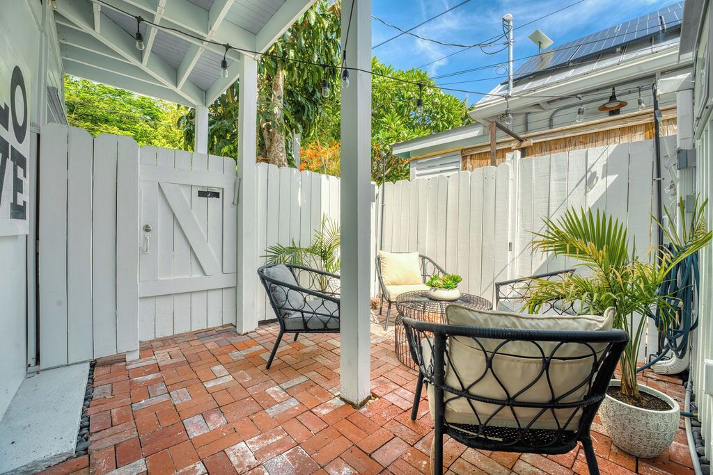 Une terrasse couverte avec un sol en briques, une clôture en bois peinte en blanc, du mobilier d’extérieur et des plantes en pot.