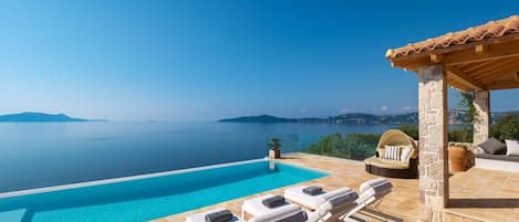 A pool with lounge chairs, a stone structure, and a view of the sea.