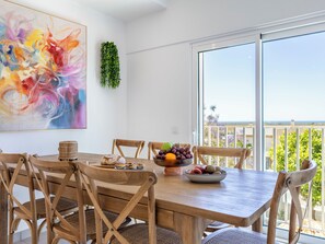 Een eetgedeelte met een houten tafel, stoelen, een fruitschaal en een kleurrijk abstract schilderij aan de muur.