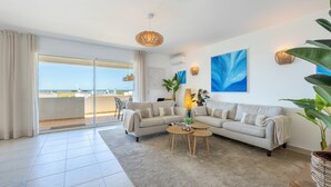A modern living room with a sofa, coffee table, and large windows overlooking a balcony. - Casa Alvor - Rooftop Jacuzzi with Sea Views (Alvor)