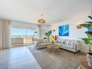 Een moderne woonkamer met een bank, salontafel en grote ramen met uitzicht op een balkon.