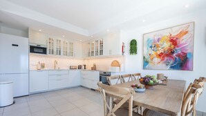 A modern kitchen with white cabinets, a dining table with wooden chairs, and a colorful abstract painting on the wall. - Casa Alvor - Rooftop Jacuzzi with Sea Views (Alvor)