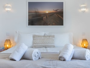 A neatly made bed with rolled white towels, a white pillow, and a framed picture of a sunset over a beach. - Apartment Alvor - Rooftop Jacuzzi with Sea Views (Alvor)
