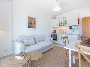 A modern living room with a sofa, a small round table with books, a dining table with chairs, a kitchen with white cabinets, and a hanging light fixture. - Apartment Alvor - Rooftop Jacuzzi with Sea Views (Alvor)