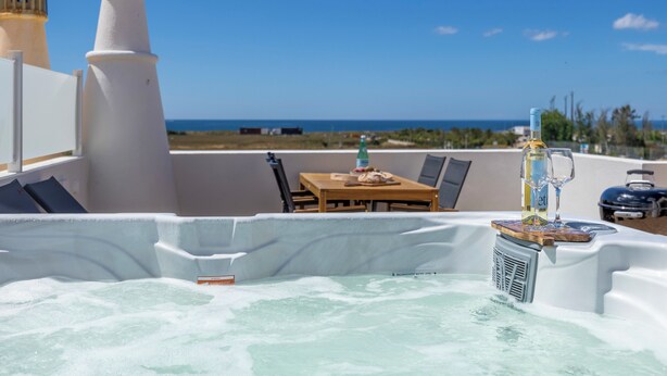 Un bain à remous avec vue sur l’océan, une table avec des chaises et une bouteille de vin.