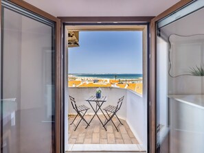En balkong med ett bord och stolar, en krukväxt och utsikt över stranden och byggnaderna.